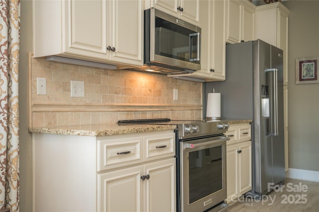 kitchen with high end appliances, cream cabinets, light stone counters, and decorative backsplash