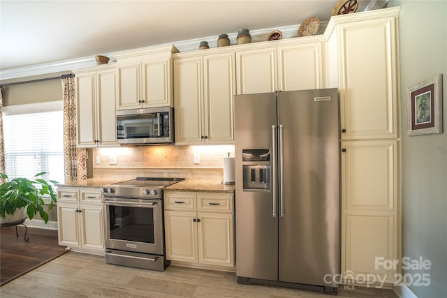 kitchen with decorative backsplash, light stone countertops, cream cabinetry, and appliances with stainless steel finishes