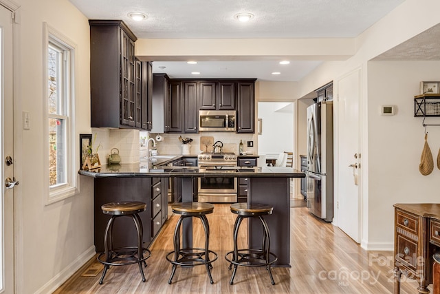 kitchen featuring appliances with stainless steel finishes, a breakfast bar, dark brown cabinetry, and light hardwood / wood-style floors