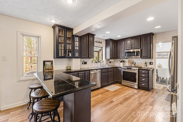 kitchen featuring appliances with stainless steel finishes, a breakfast bar area, backsplash, kitchen peninsula, and dark brown cabinets