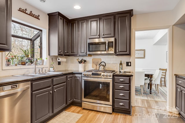 kitchen with sink, stainless steel appliances, dark brown cabinetry, tasteful backsplash, and light hardwood / wood-style floors