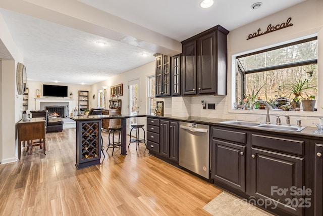 kitchen featuring tasteful backsplash, dishwasher, sink, dark brown cabinets, and light hardwood / wood-style flooring