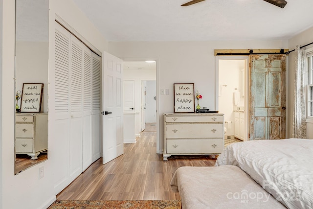 bedroom featuring ensuite bath, light wood-type flooring, a closet, ceiling fan, and a barn door