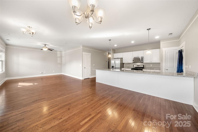 kitchen featuring appliances with stainless steel finishes, hanging light fixtures, light stone countertops, white cabinets, and ceiling fan with notable chandelier