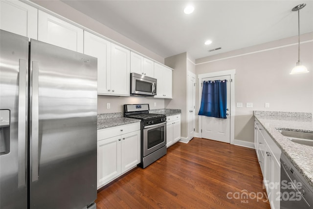 kitchen with appliances with stainless steel finishes, white cabinetry, hanging light fixtures, dark hardwood / wood-style floors, and light stone counters