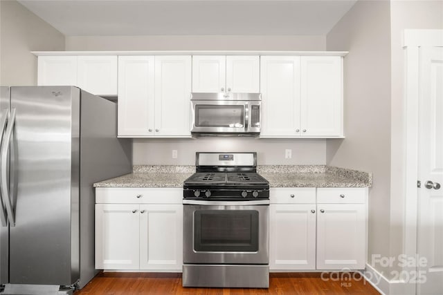 kitchen with stainless steel appliances, white cabinetry, light stone countertops, and wood-type flooring