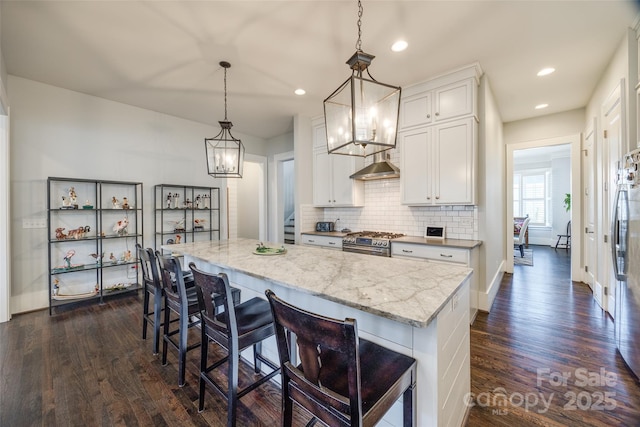 kitchen with white cabinetry, decorative light fixtures, a kitchen island, stainless steel appliances, and light stone countertops