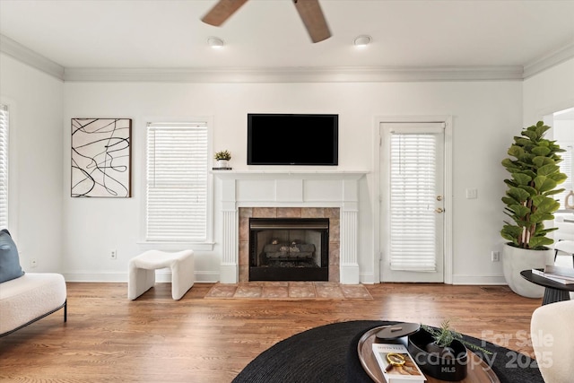 living room featuring a tiled fireplace, ornamental molding, ceiling fan, and light hardwood / wood-style floors