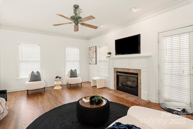 living room with crown molding, wood-type flooring, a tile fireplace, and a wealth of natural light