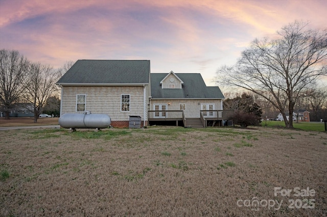 back house at dusk featuring a wooden deck and a lawn