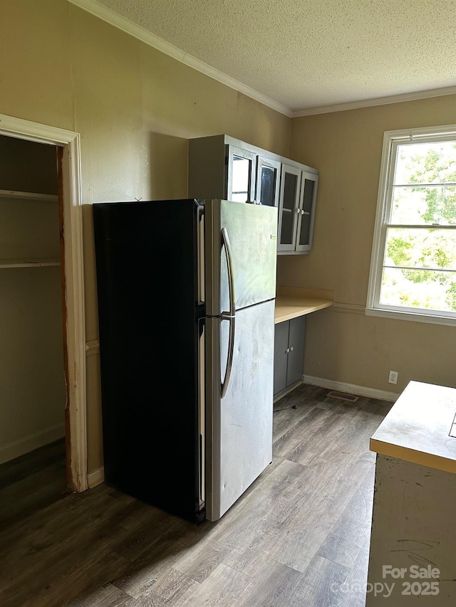 kitchen with stainless steel refrigerator, ornamental molding, wood-type flooring, and a textured ceiling