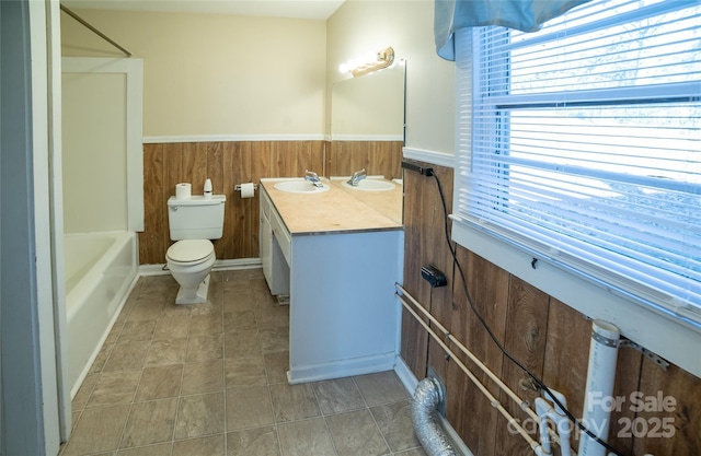 full bathroom featuring vanity, wood walls, washtub / shower combination, and toilet