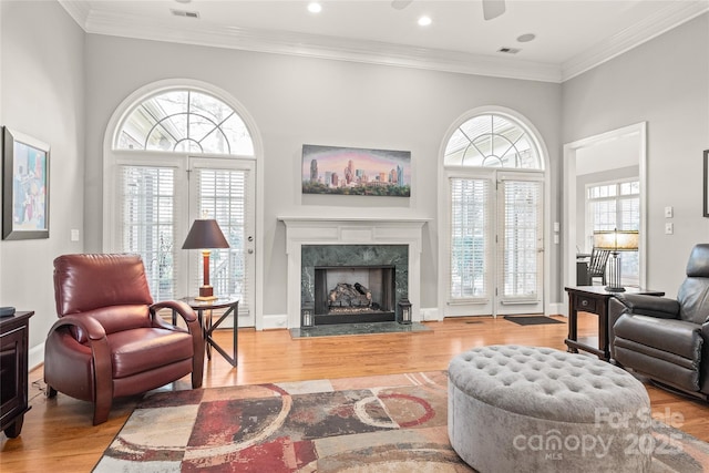 living room featuring crown molding, a premium fireplace, a wealth of natural light, and light wood-type flooring