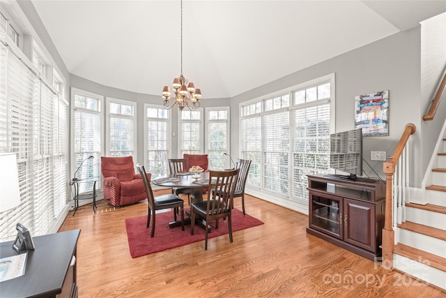 dining area with a healthy amount of sunlight, a chandelier, vaulted ceiling, and light wood-type flooring