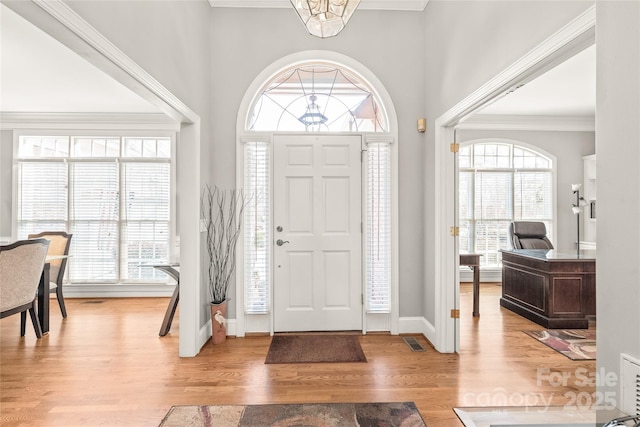 foyer entrance featuring crown molding, an inviting chandelier, and light wood-type flooring