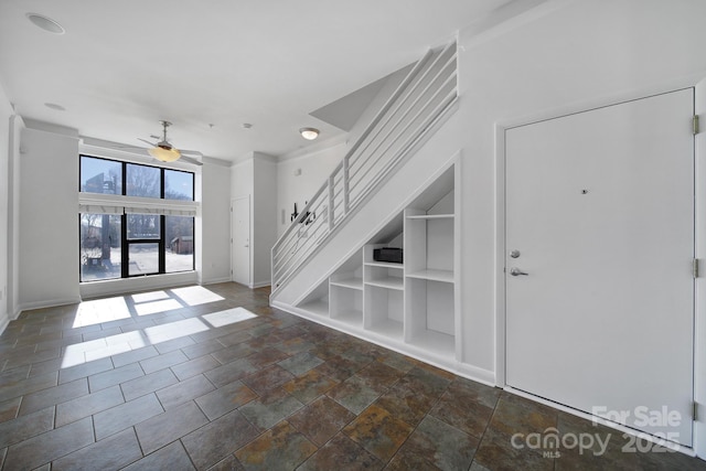 interior space with baseboards, built in features, ceiling fan, stone finish flooring, and stairs