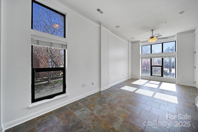 empty room with baseboards, visible vents, a ceiling fan, and stone finish flooring