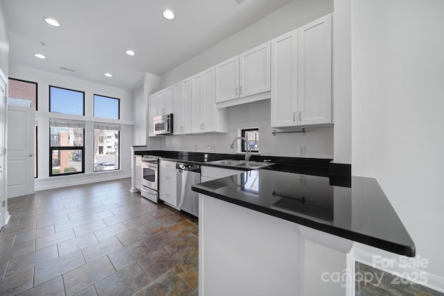 kitchen featuring white cabinets, dark countertops, appliances with stainless steel finishes, a sink, and a wealth of natural light