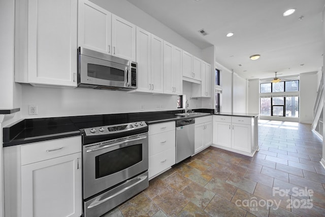 kitchen featuring stainless steel appliances, dark countertops, visible vents, white cabinets, and a sink