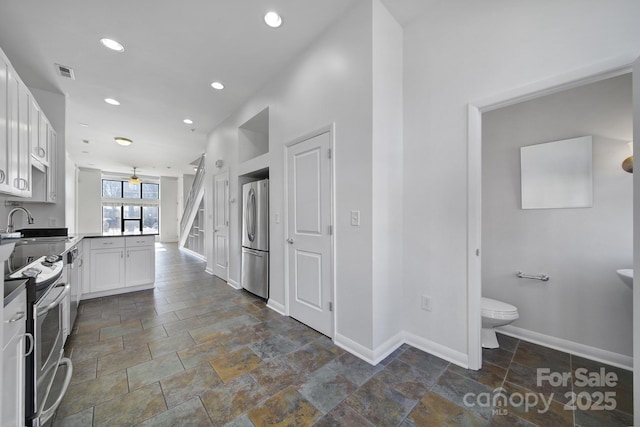 kitchen with stone tile floors, stainless steel appliances, visible vents, white cabinets, and baseboards