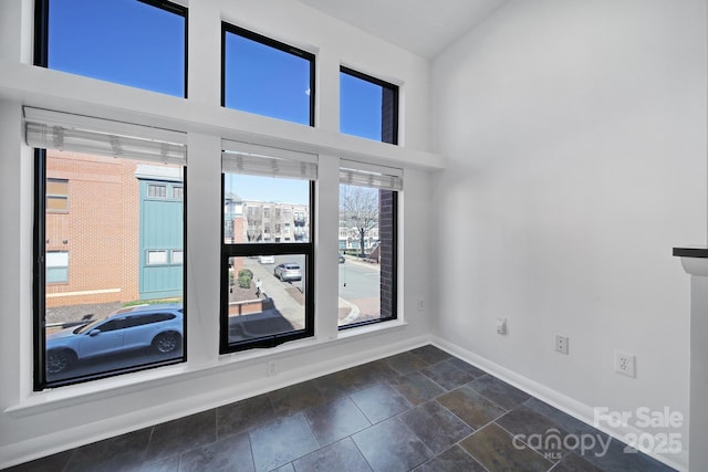 empty room featuring a towering ceiling, stone tile floors, and baseboards