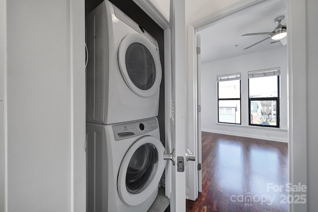 laundry room featuring laundry area, baseboards, a ceiling fan, stacked washer / dryer, and dark wood-style flooring