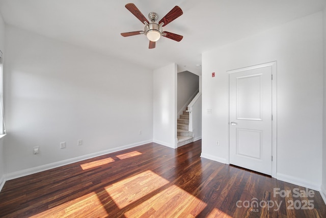 empty room featuring ceiling fan, stairs, baseboards, and wood finished floors