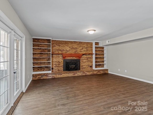 unfurnished living room with dark wood-type flooring, built in shelves, and a brick fireplace