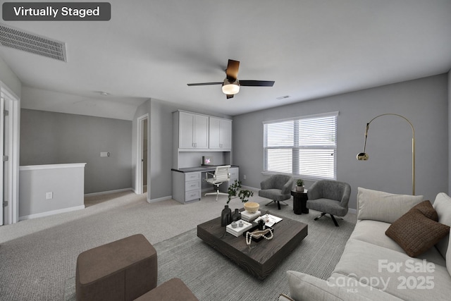 living room with built in desk, light carpet, and ceiling fan