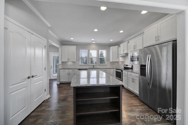 kitchen with appliances with stainless steel finishes, a kitchen island, white cabinets, light stone countertops, and backsplash