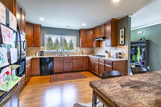 kitchen featuring decorative backsplash, light wood-style floors, a sink, under cabinet range hood, and black appliances