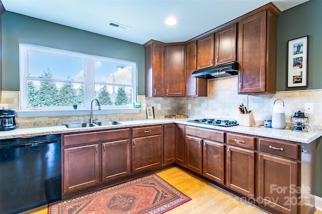 kitchen with black dishwasher, light wood-style flooring, a sink, gas cooktop, and under cabinet range hood