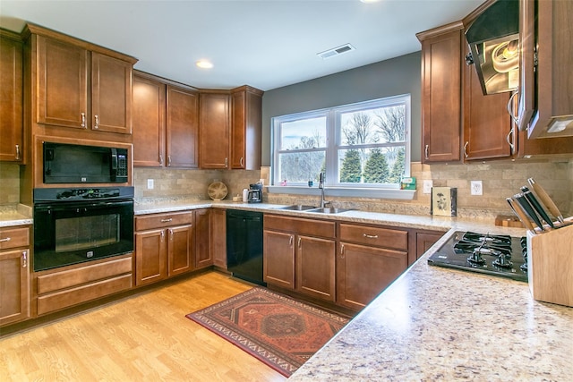 kitchen featuring tasteful backsplash, visible vents, light wood-style floors, a sink, and black appliances