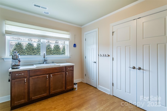 kitchen with ornamental molding, visible vents, a sink, and light wood-style flooring