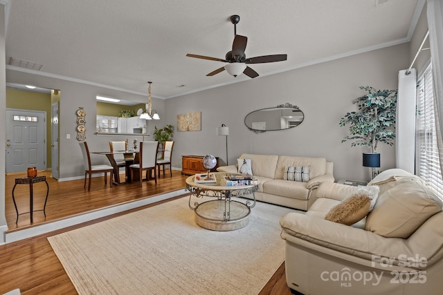 living room featuring hardwood / wood-style flooring, ornamental molding, ceiling fan, and a textured ceiling