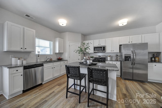 kitchen with a kitchen island, appliances with stainless steel finishes, a breakfast bar, white cabinetry, and dark stone countertops