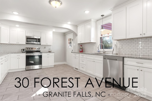 kitchen with sink, white cabinetry, hanging light fixtures, stainless steel appliances, and light stone countertops