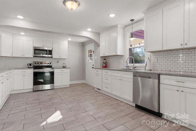 kitchen with white cabinetry, stainless steel appliances, decorative light fixtures, and sink