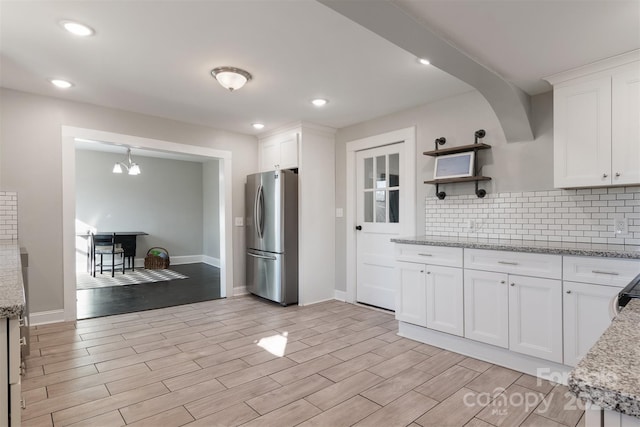 kitchen featuring stainless steel refrigerator, backsplash, a chandelier, white cabinets, and light stone counters