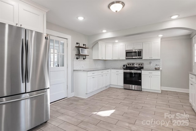 kitchen with light stone countertops, appliances with stainless steel finishes, white cabinets, and decorative backsplash