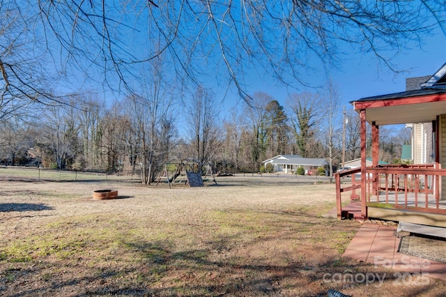 view of yard featuring a wooden deck, a playground, and an outdoor fire pit