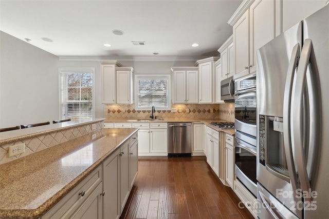 kitchen with sink, white cabinetry, backsplash, stainless steel appliances, and light stone countertops