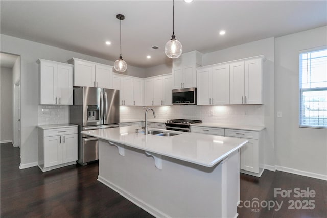 kitchen featuring pendant lighting, sink, stainless steel appliances, an island with sink, and white cabinets