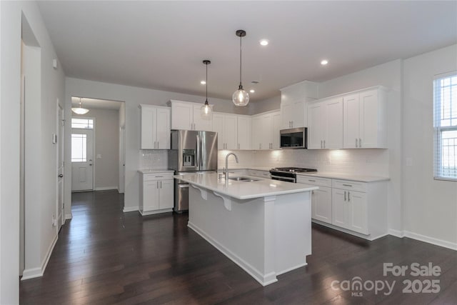 kitchen with stainless steel appliances, an island with sink, white cabinets, and decorative light fixtures