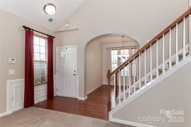 carpeted entrance foyer with plenty of natural light, lofted ceiling, and an inviting chandelier