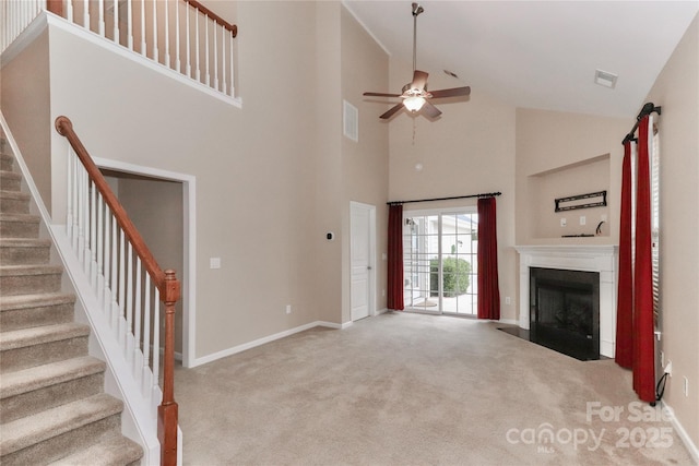 unfurnished living room with ceiling fan, a towering ceiling, and light colored carpet