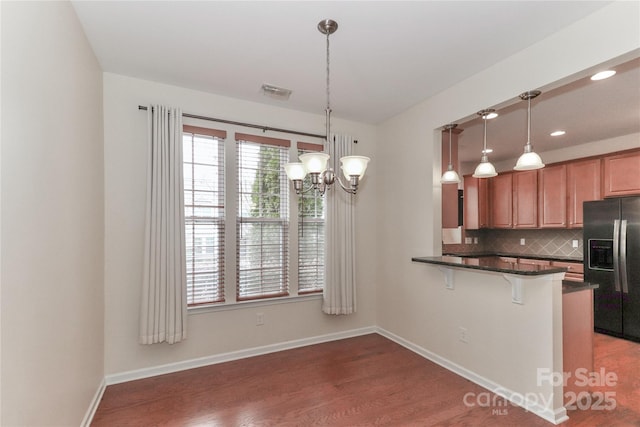 kitchen with pendant lighting, tasteful backsplash, black fridge with ice dispenser, and kitchen peninsula