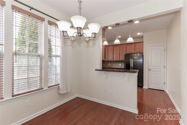 kitchen featuring pendant lighting, stainless steel fridge, kitchen peninsula, and decorative backsplash