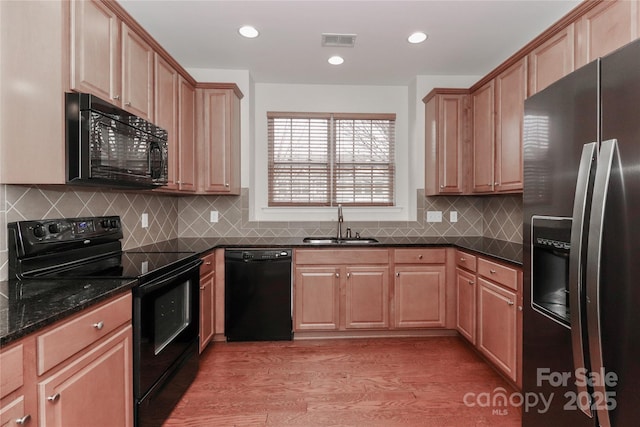 kitchen featuring sink, decorative backsplash, dark stone counters, black appliances, and light hardwood / wood-style flooring