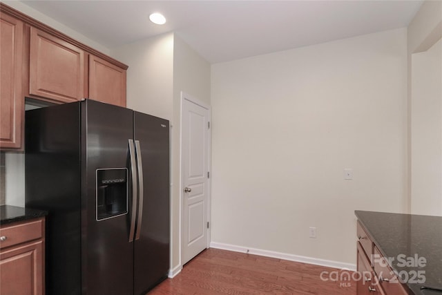 kitchen with dark hardwood / wood-style floors, black refrigerator with ice dispenser, and dark stone counters